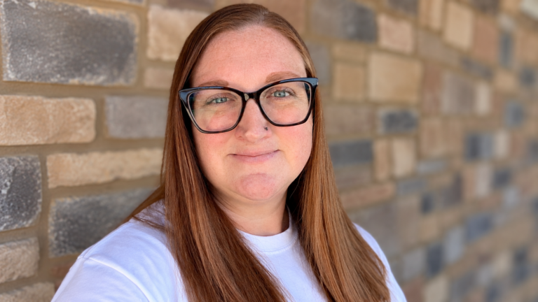 Courtney Soltau, a 2003 Stautzenberger College Veterinary Technology graduate, wearing black-framed glasses and smiling in front of a stone wall.